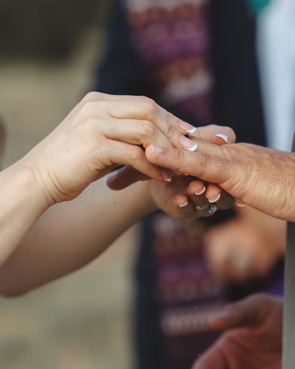 Close-up of bride placing wedding ring on grooms finger during outdoor wedding ceremony.