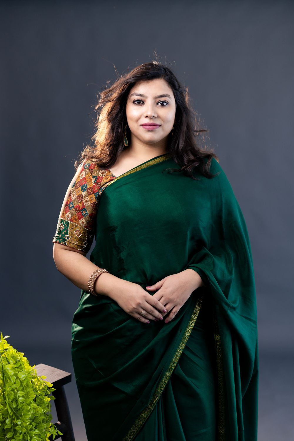 Woman in elegant dark green saree with embroidered blouse, posing confidently in a studio setting.