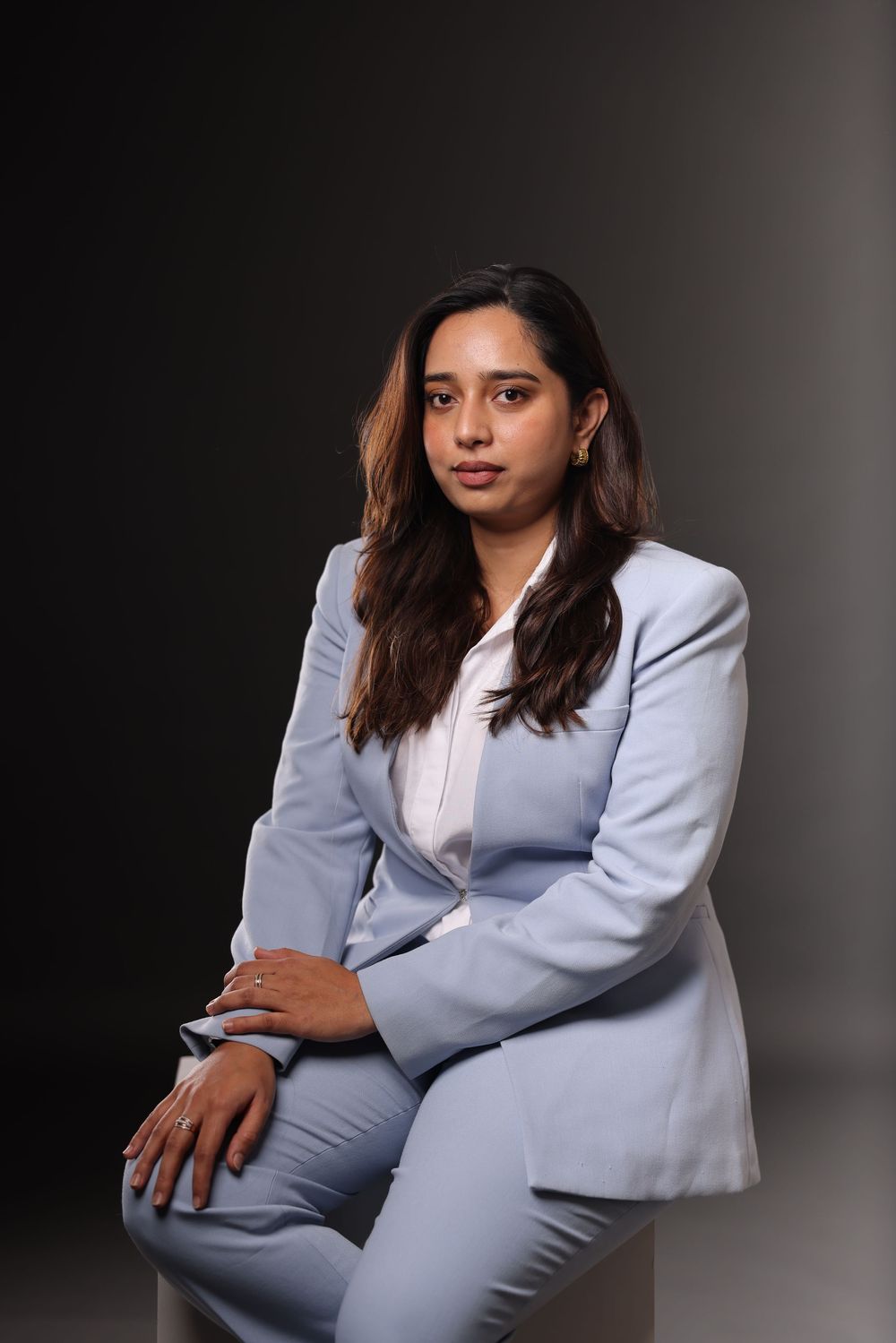 Professional woman in light blue suit seated confidently against dark background for corporate portrait.