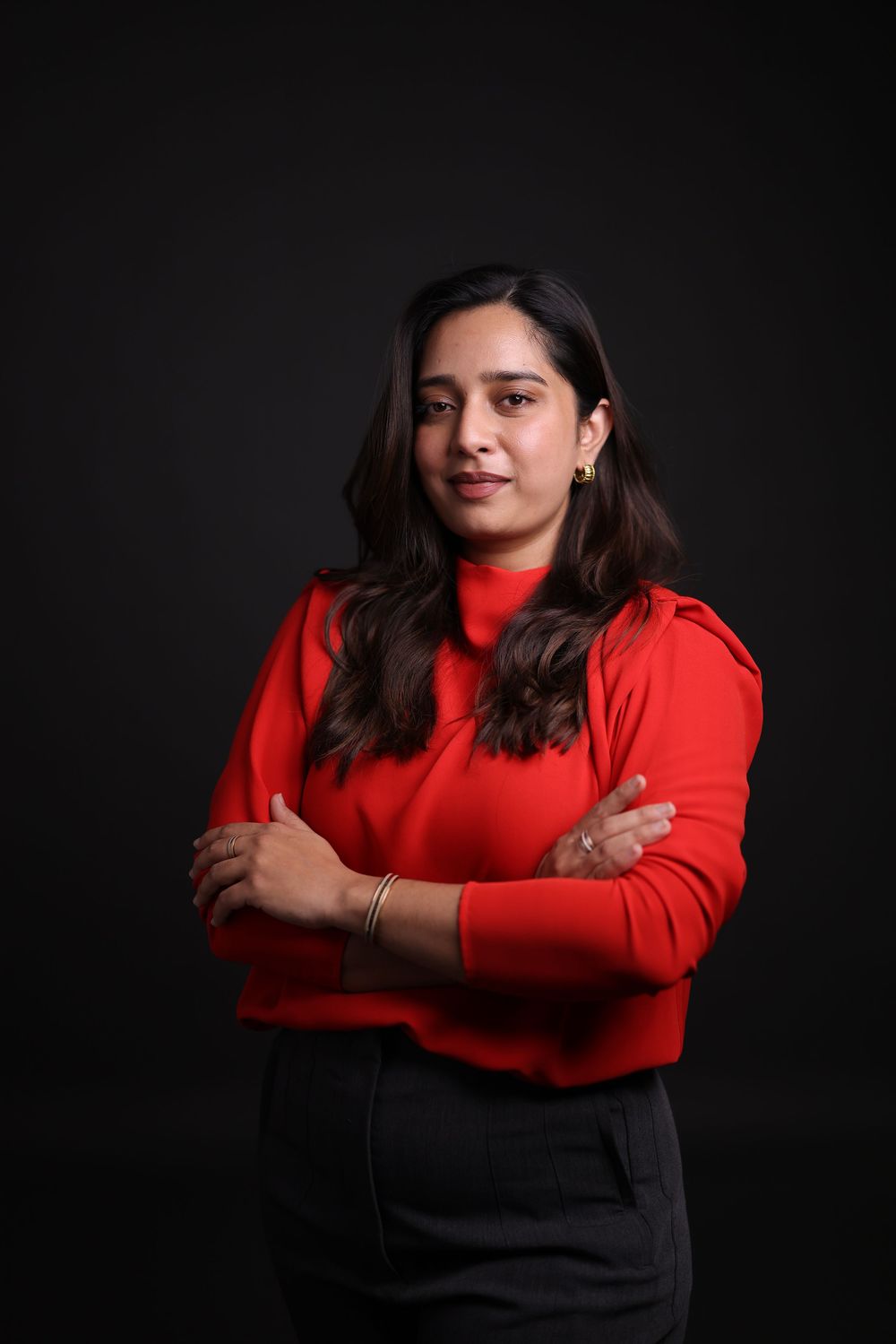 A confident woman in a red turtleneck sweater poses with arms crossed against a dark background.