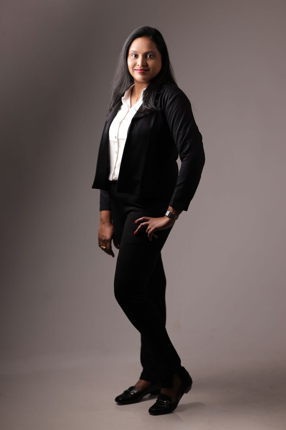 Professional woman in black blazer and trousers posing confidently in a studio setting.