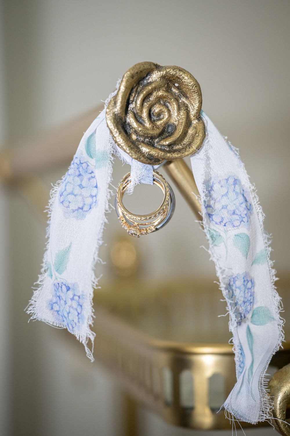 Gold rose curtain rod finial with a white floral fabric ribbon and gold ring accent, elegant home decor detail.