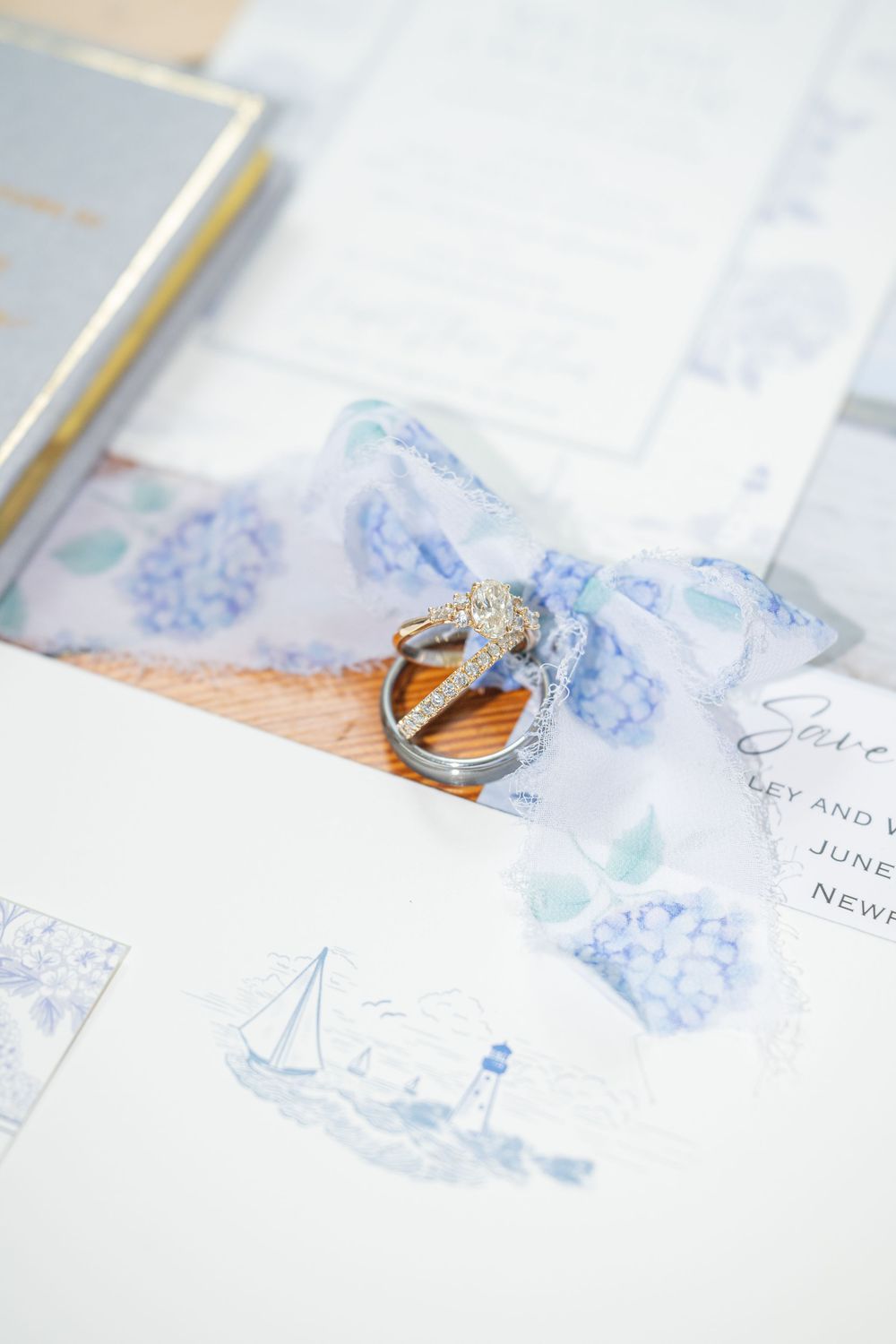 Wedding rings resting on blue hydrangea save-the-date cards with sheer ribbon, elegant nautical stationery suite.