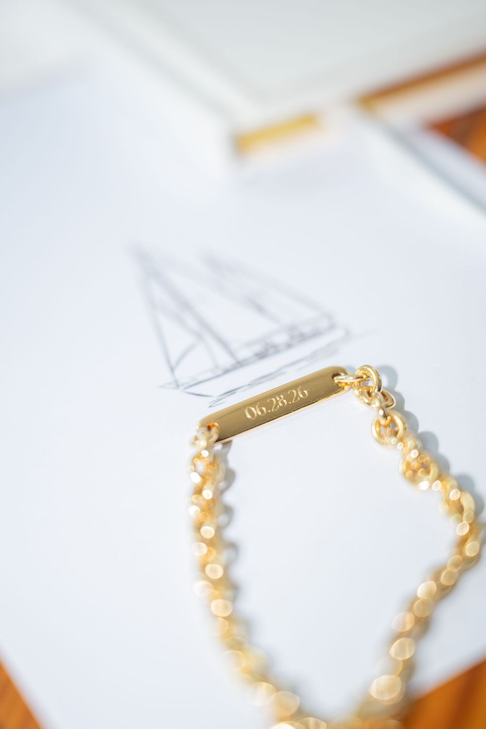 Gold engraved date bar bracelet with pearl chain resting on wedding dress sketch drawing.
