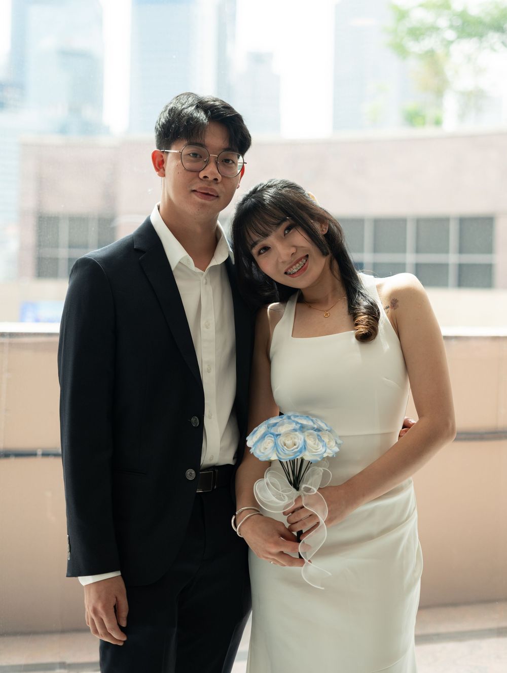 Couple posing in wedding attire, groom in black suit and bride in white dress holding blue bouquet.
