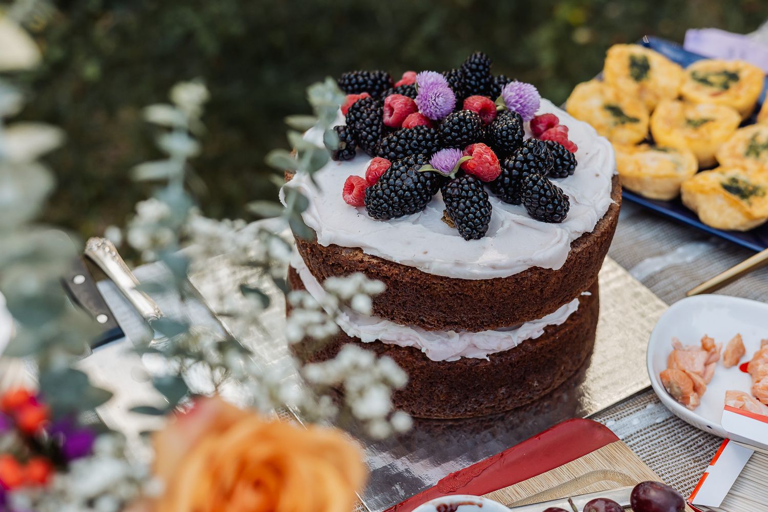 Rustic naked cake topped with fresh blackberries and raspberries on a outdoor dessert table.