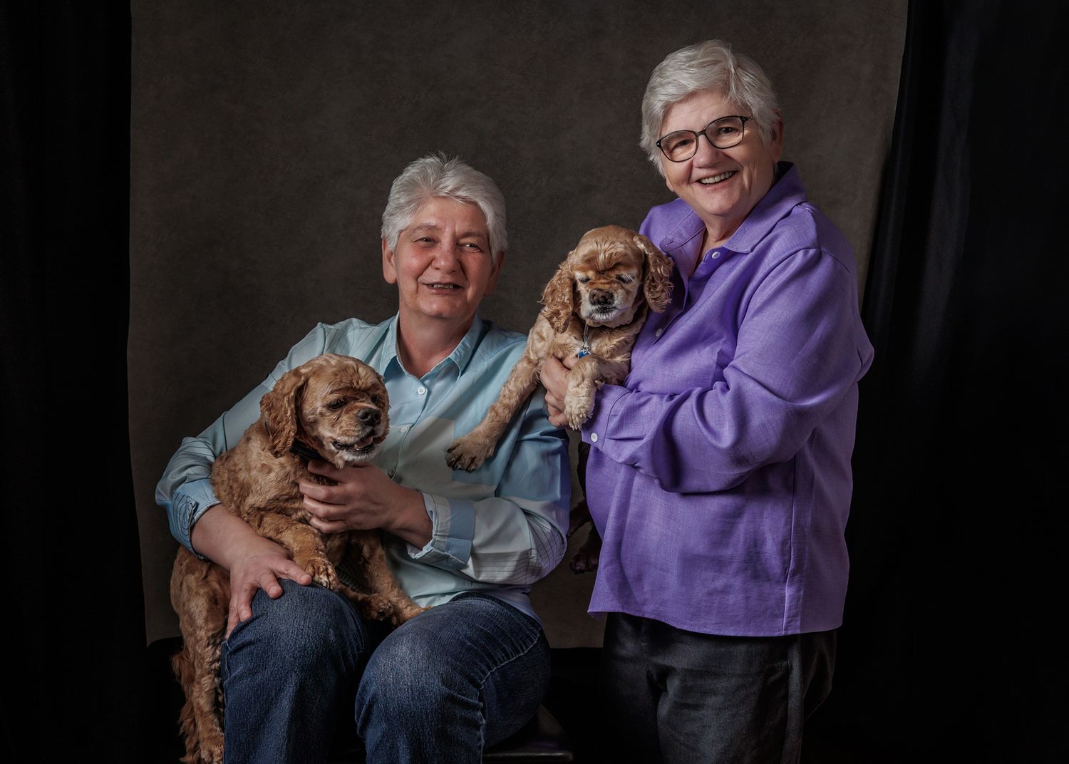 Two smiling senior women holding adorable Cocker Spaniel dogs pose together for a portrait photo.