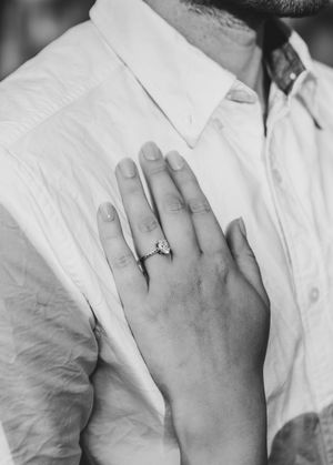 Black and white photo of a woman's hand with a diamond engagement ring resting on a man's white dress shirt.