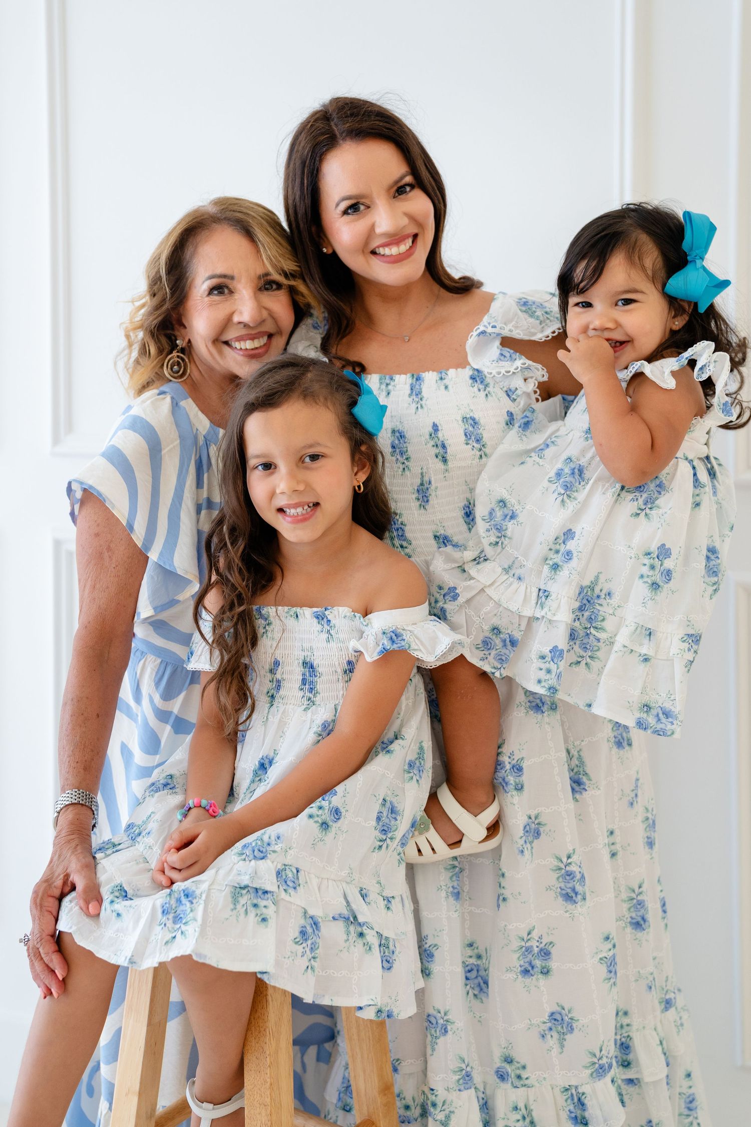 Four females in matching blue floral dresses pose together for a cheerful family portrait against a white background.