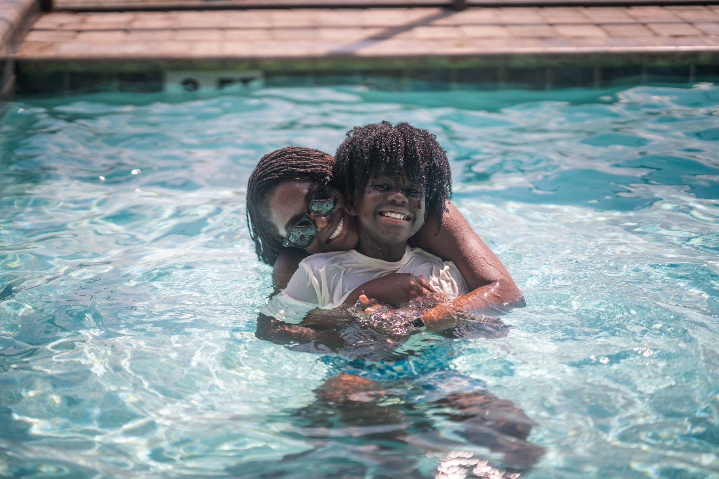 Two children joyfully hugging in a swimming pool, smiling and playing together on a sunny day.