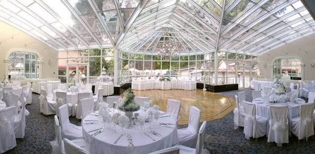 A bright glass conservatory wedding venue with white chair covers and round tables set for an elegant reception.