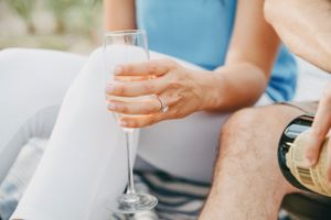 Close-up of woman holding champagne flute with engagement ring while partner pours bubbly.