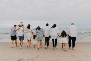 Large family holding hands walking toward ocean beach together in coordinated white and blue outfits.