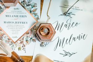 Wedding stationery flat lay featuring floral invitations, ring box with diamond ring, and elegant calligraphy program.