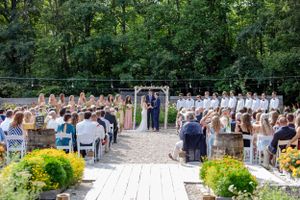 Outdoor garden wedding ceremony with guests seated along aisle surrounded by lush green trees.