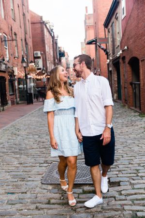A smiling couple holding hands and walking together on a charming cobblestone street.