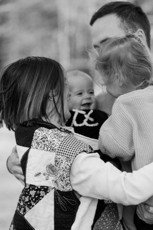 Black and white family photo of parents embracing laughing baby and young children outdoors.