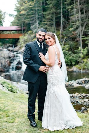 Bride and groom posing together in front of waterfall and covered bridge at wedding venue.