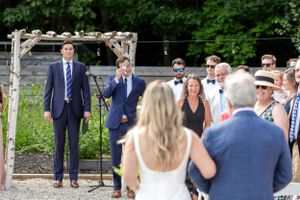 Groom emotional at altar watching bride walk down outdoor aisle at rustic garden wedding.