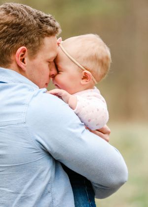 Tender moment of father touching foreheads with baby dressed in pink outfit in outdoor setting.
