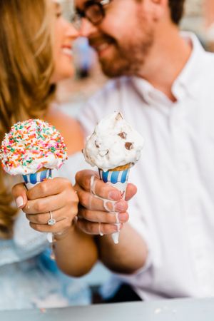 Couple smiling and holding colorful ice cream cones with sprinkles on a sunny day.