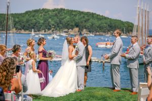 Bride and groom share first kiss at outdoor waterfront wedding ceremony with bridal party.