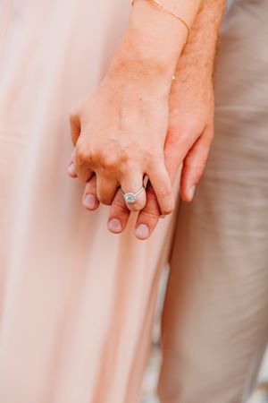 Close-up of couple holding hands showing elegant diamond engagement ring on brides finger.