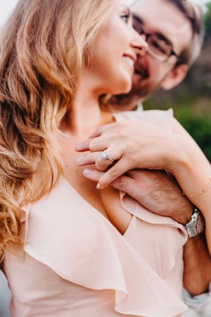 A close-up of a couple embracing with a sparkling engagement ring prominently displayed on her hand.
