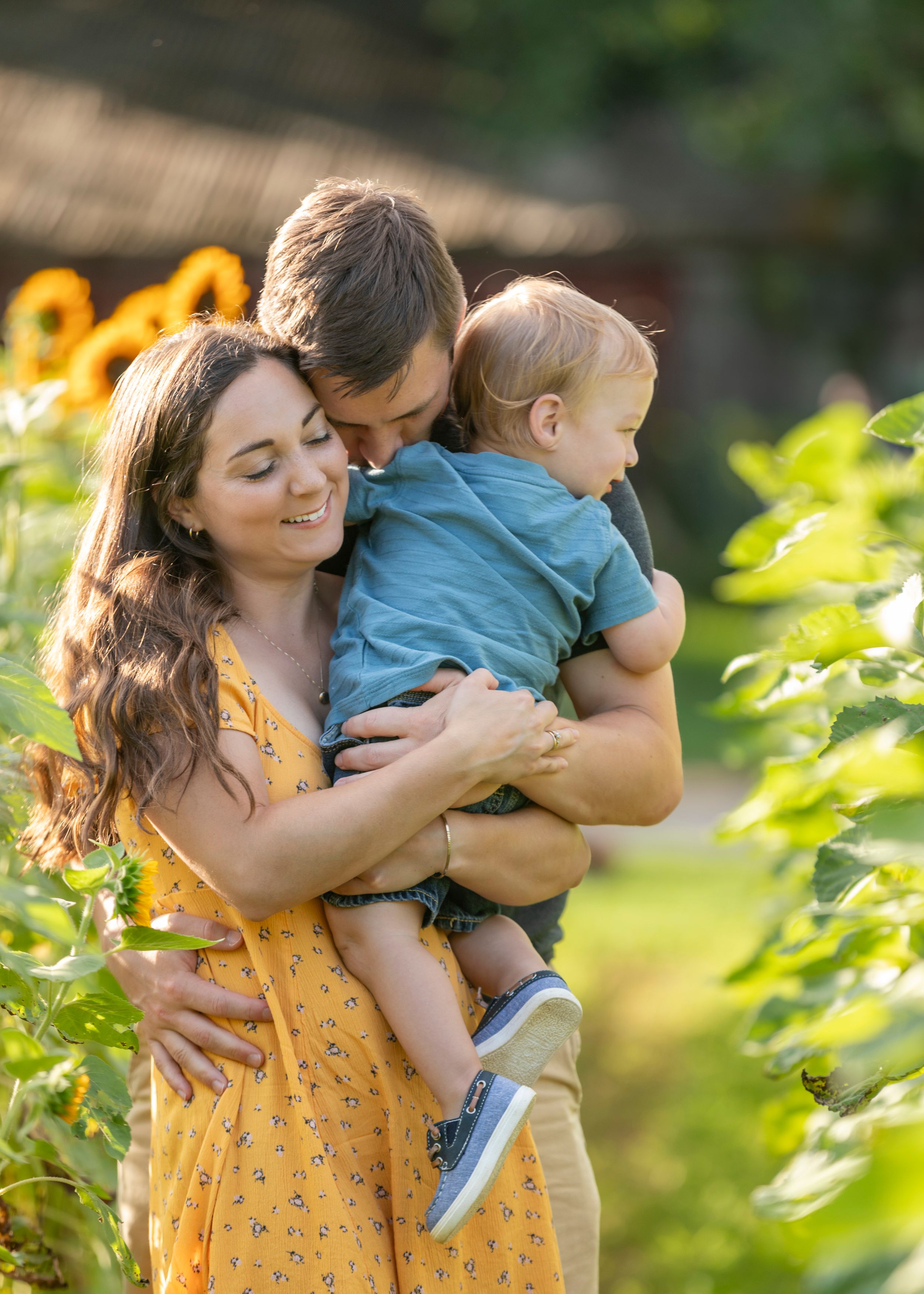 Happy young family with toddler embracing in a sunflower garden during golden hour outdoor portrait session.