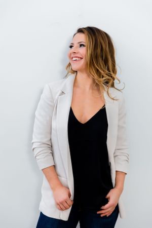 A smiling woman in a white blazer and black top posing confidently against a white background.