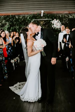 Bride and groom kissing at altar in front of lush green floral wall at elegant wedding.