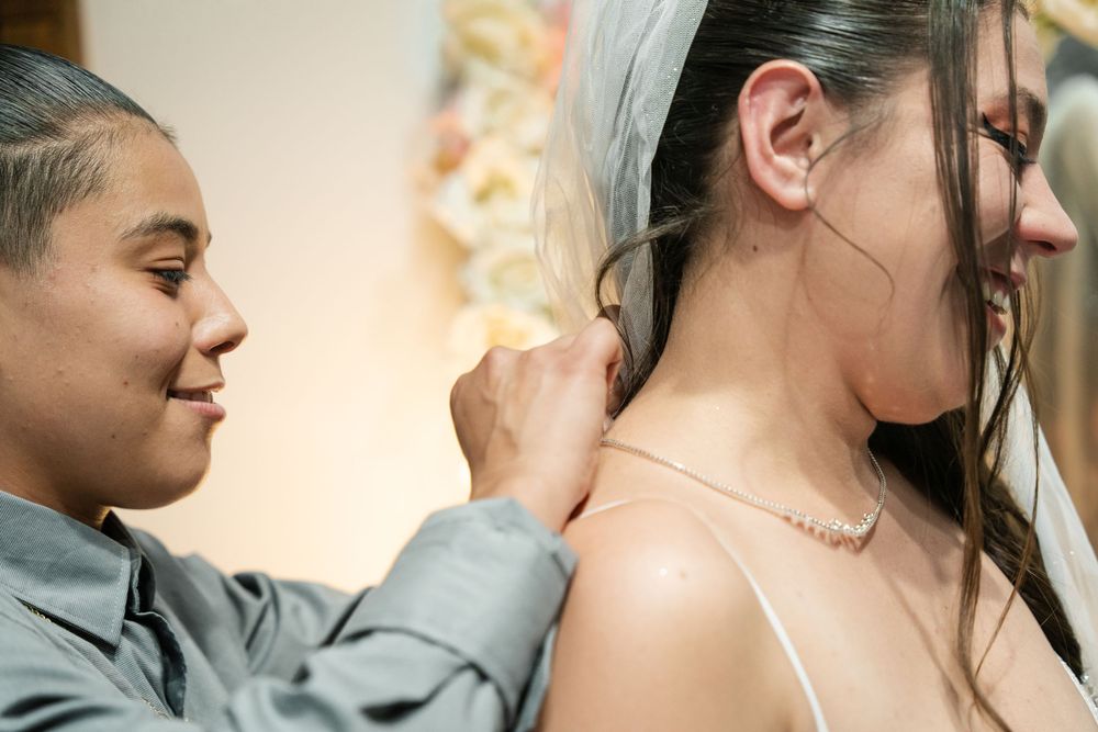 Bridesmaid helping bride with pearl necklace clasp before wedding ceremony.