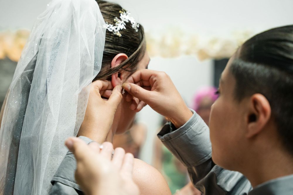Bridesmaid carefully placing earring on bride wearing floral veil.
