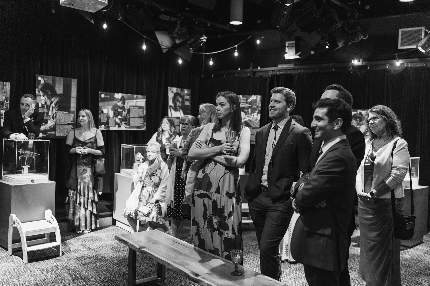 Black and white photo of elegantly dressed guests viewing artwork at an indoor gallery exhibition event.
