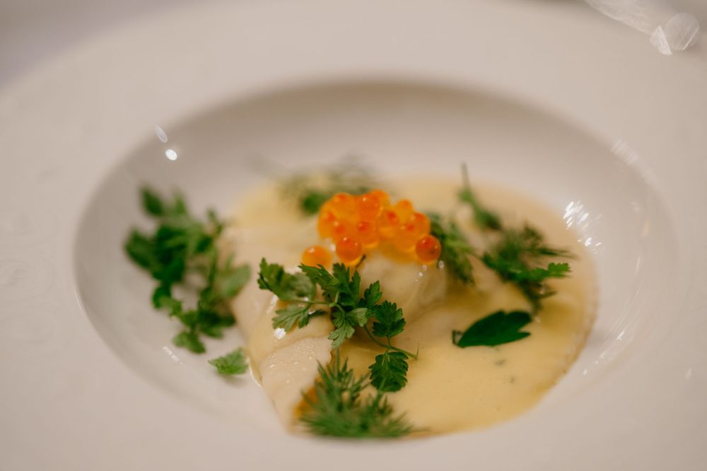 Delicate scallop dish with orange roe and fresh herbs in a cream sauce.