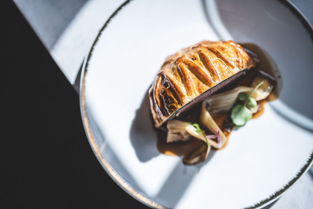 Elegantly plated pastry dish with mushrooms on a white plate in soft light.
