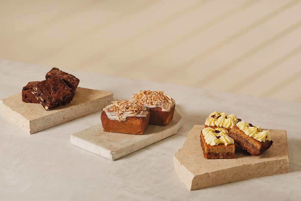 Three assorted cake slices displayed on marble boards against a neutral background.