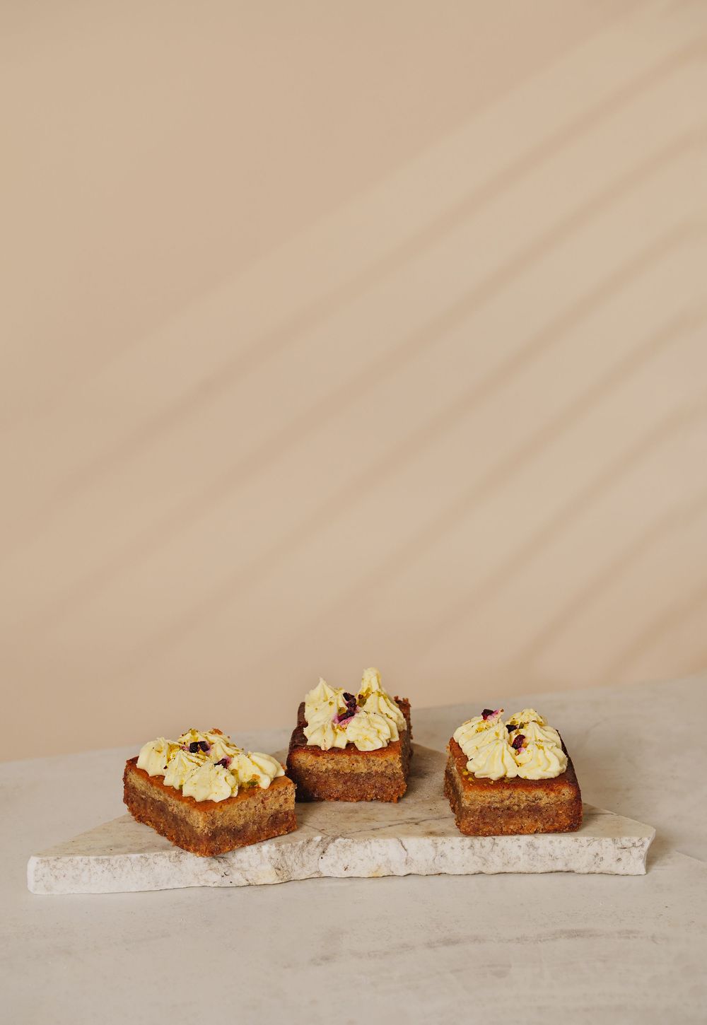 Four square carrot cake slices topped with cream cheese frosting on a marble board.