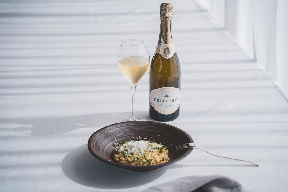 Creamy risotto with Parmesan beside Petit Jete sparkling wine bottle and glass.