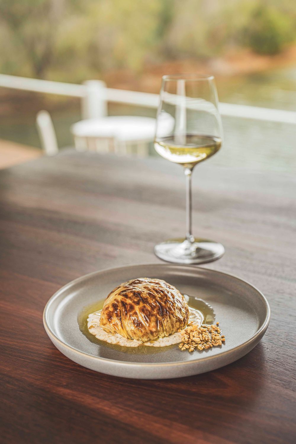 Roasted cauliflower with white sauce and granola on a ceramic plate paired with a glass of white wine.