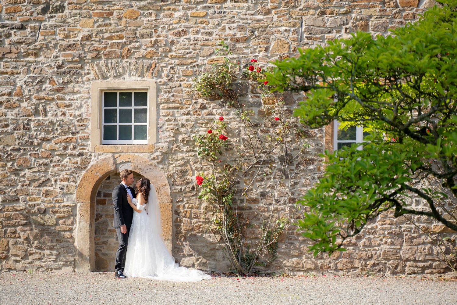 Bride and groom kissing under stone arch of rustic castle wedding venue with climbing roses.