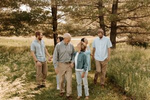 A family of five walks together among tall pine trees in a lush green meadow.