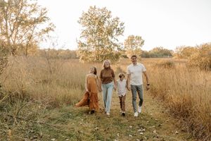 Family of four walking through golden autumn fields on a sunny day, smiling and holding hands.