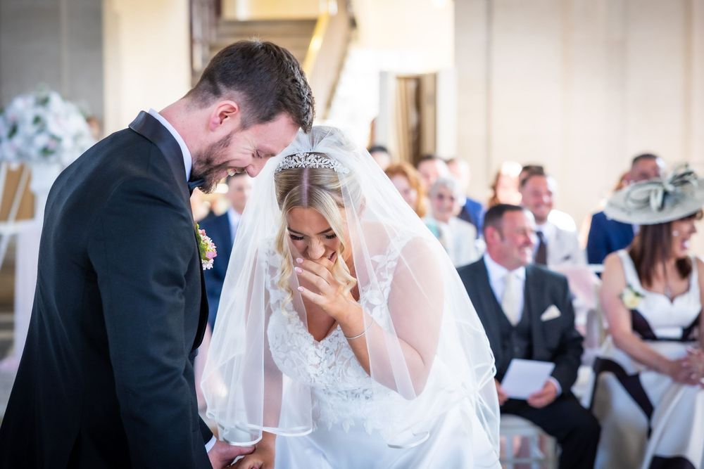 Emotional bride and groom sharing a tender moment during wedding ceremony, bride in lace gown and veil covering her face.