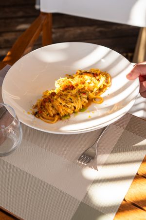 Plate of fresh egg pasta with sauce served on a white dish in sunlight at a restaurant table.
