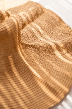Close-up of a golden tan woven bucket hat brim with subtle stripe texture in warm sunlight.