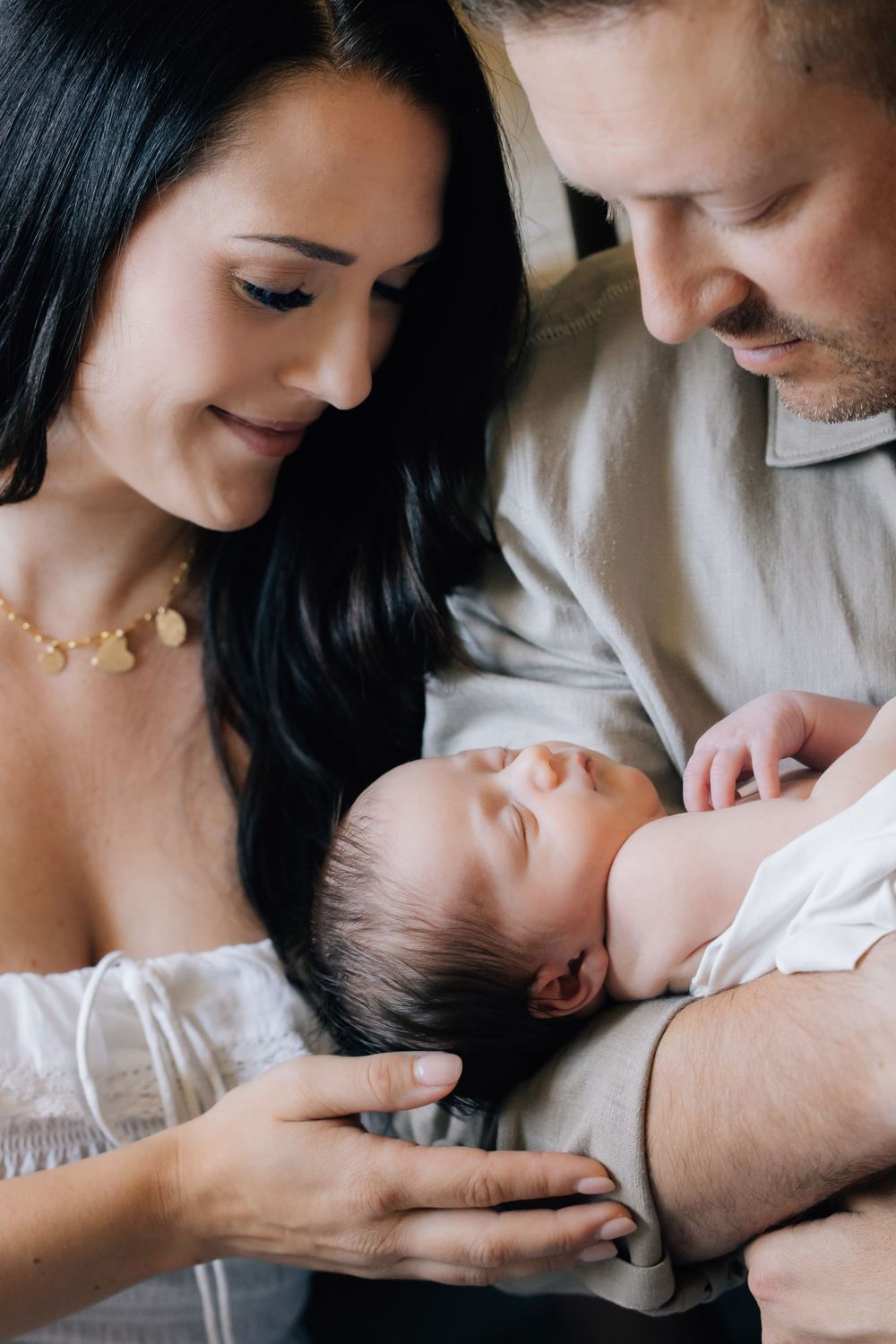 Parents tenderly cradling their sleeping newborn baby together in a close family portrait.