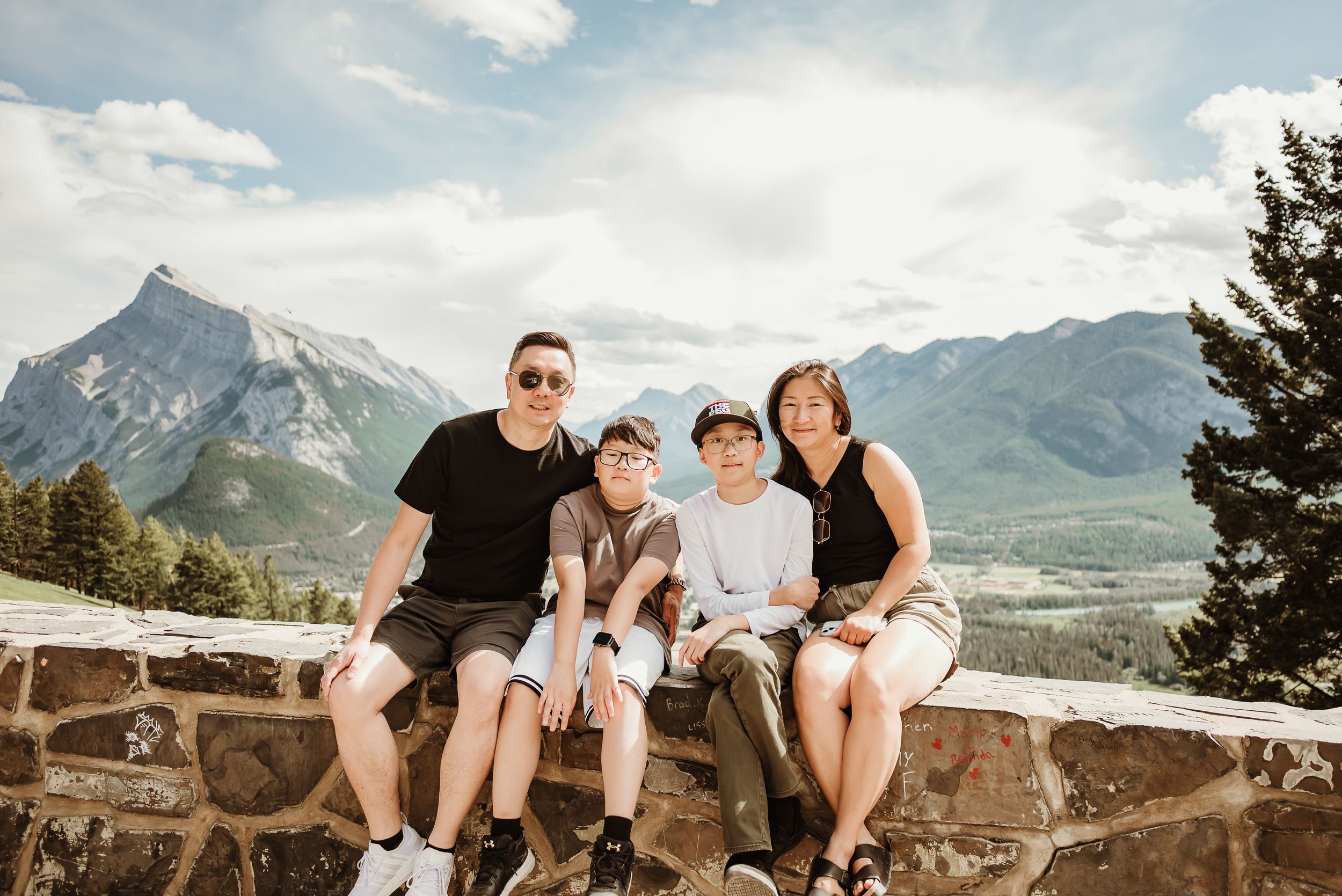 A group sits together on a rocky outcrop overlooking majestic mountain peaks in the scenic Canadian Rockies.