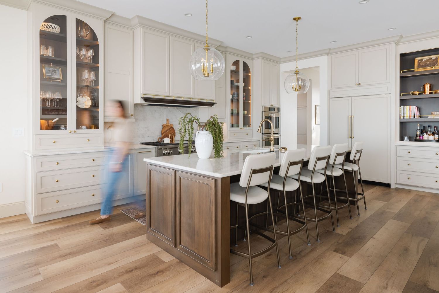 Modern white kitchen with wood floors features pendant lights and built-in cabinetry.
