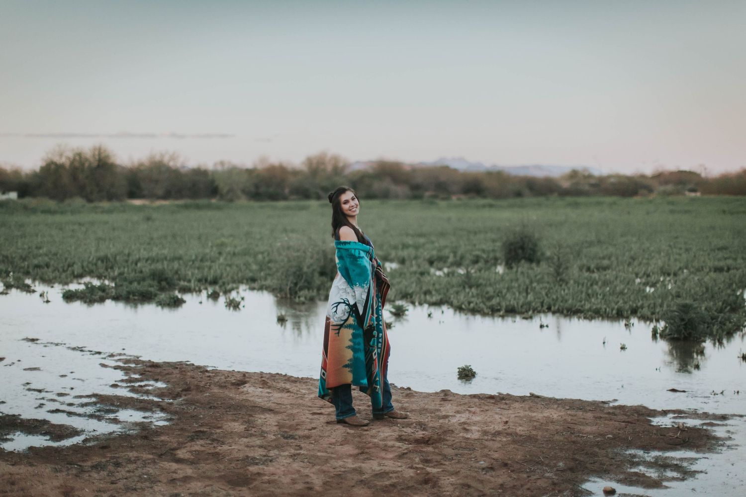 Figure in teal outfit standing near water reflection in grassy landscape.